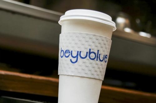 To-go coffee cup with Beyu Blue coffee sleeve and espresso machine