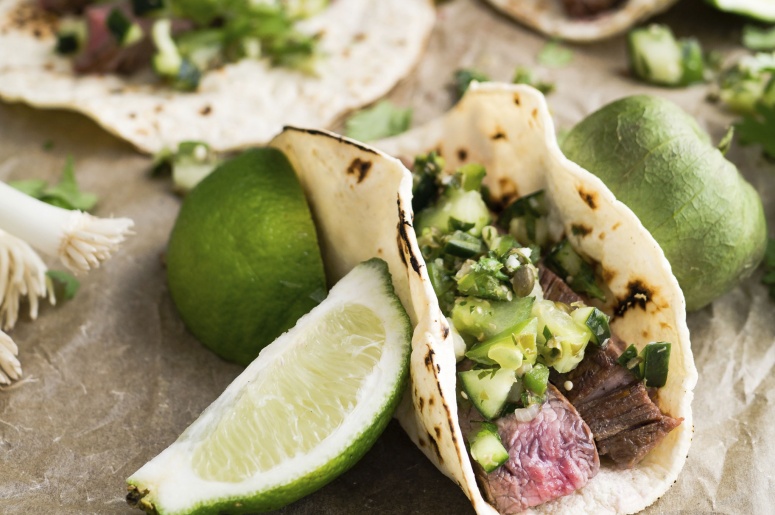 Tacos with meet, and green salsa with lime slices and a tomatillo