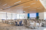 Photo of Penn Pavilion Room showing round tables, chairs, stage, windows, and projection screen.